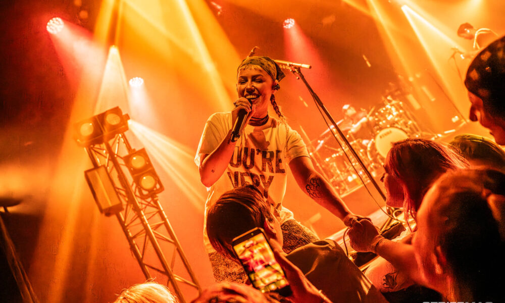 Male singer on stage under orange lights, holding a microphone and engaging with the crowd