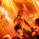 Male singer on stage under orange lights, holding a microphone and engaging with the crowd