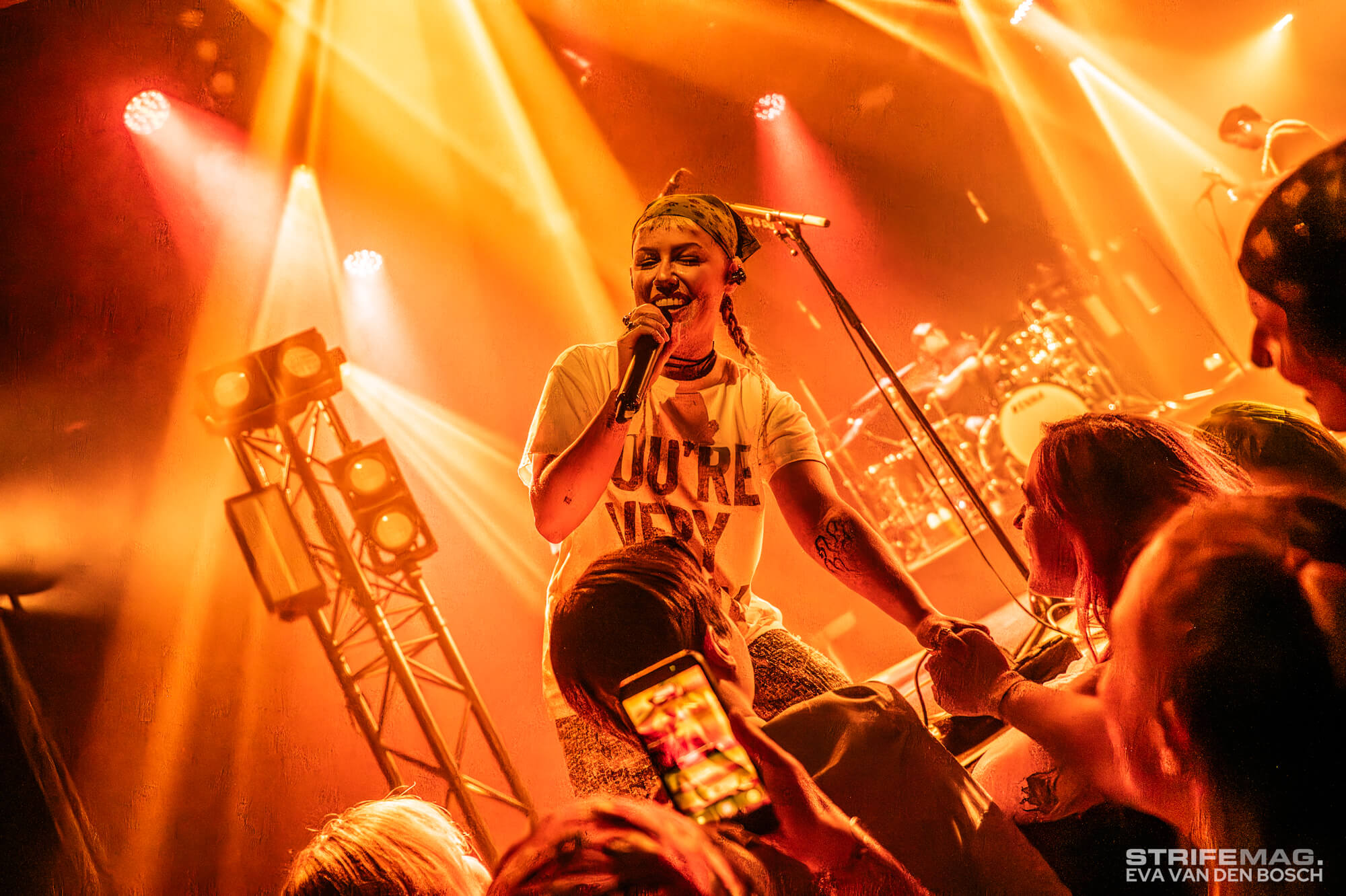 Male singer on stage under orange lights, holding a microphone and engaging with the crowd