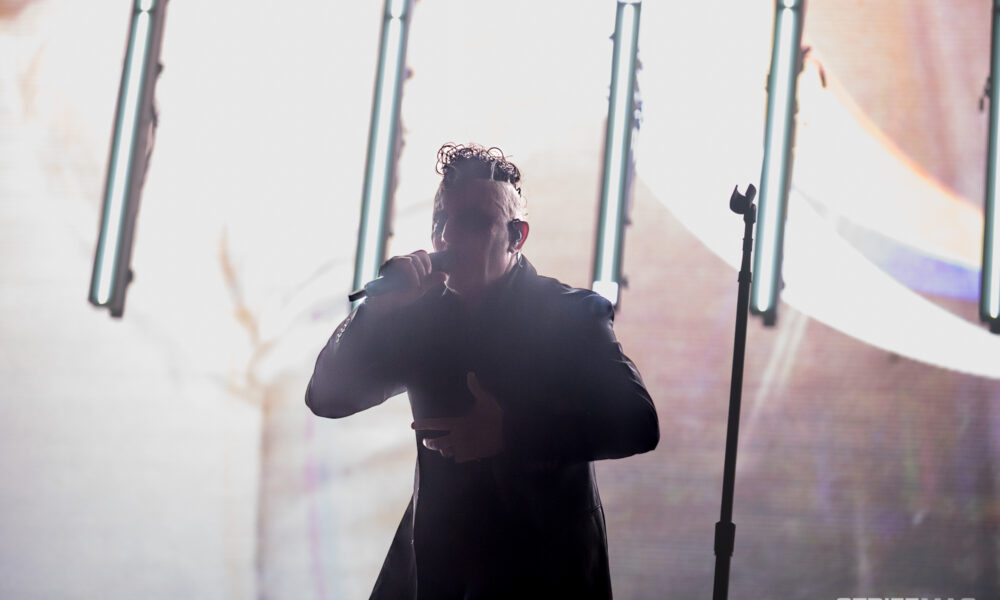 Singer performing on stage, holding a microphone with bright vertical lights behind for a dramatic concert scene.