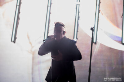 Singer performing on stage, holding a microphone with bright vertical lights behind for a dramatic concert scene.