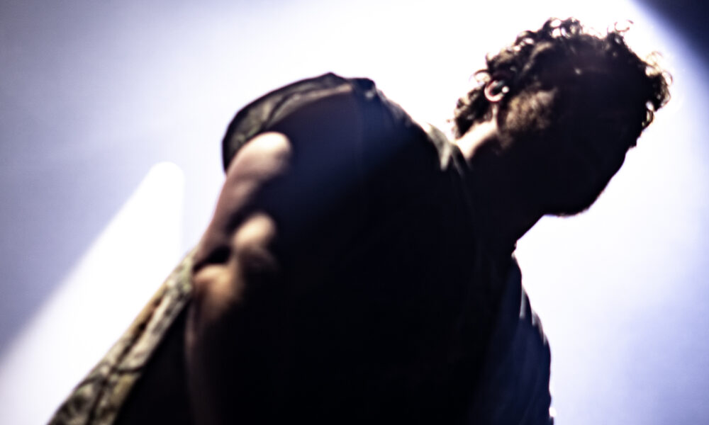 Low-angle shot of a performer on stage, backlit by a bright light, with a watermark in the bottom-right corner.