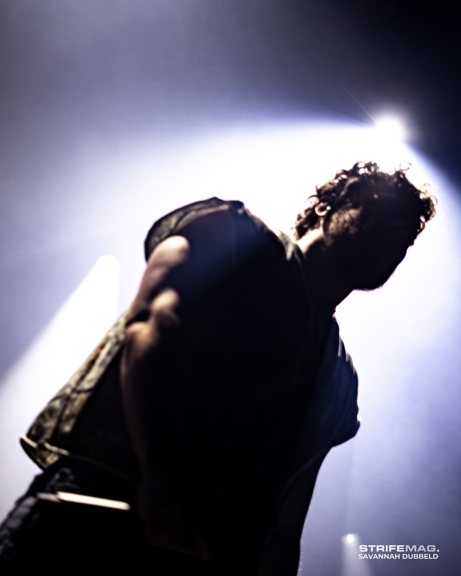 Low-angle shot of a performer on stage, backlit by a bright light, with a watermark in the bottom-right corner.