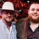 Two men posing at an event; one in a light suit with a white cowboy hat, the other in a plaid blazer.