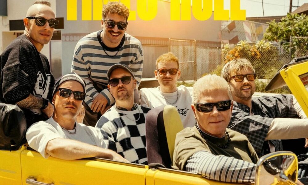 Group of men in sunglasses riding in a bright yellow convertible on a sunny street, posing for a casual band photo.