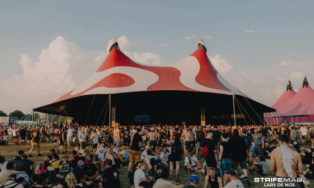 Large crowd at an outdoor festival in front of a red-and-white striped circus tent stage.
