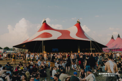 Large crowd at an outdoor festival in front of a red-and-white striped circus tent stage.